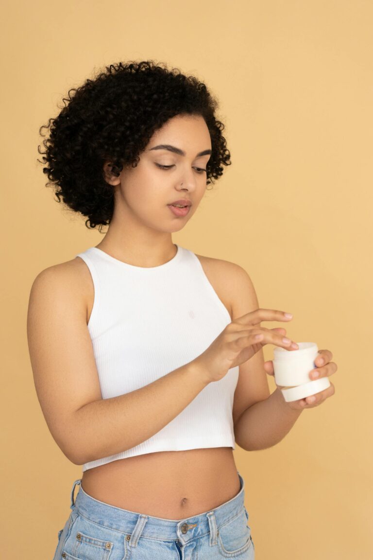 Woman with curly hair applying skincare product in a studio setting.